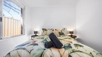 Une chambre à coucher avec un lit, deux tables de chevet, une fenêtre et une vue sur l’extérieur.
