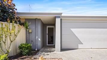 Une maison moderne de plain-pied, dotée d’un garage, d’un petit jardin devant et offrant une vue sur un ciel dégagé.