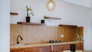 A modern kitchen with wooden cabinets, a black faucet, a gas stove, and a hanging light fixture. - Ramasita Villa by Bali Sukha (Ubud)