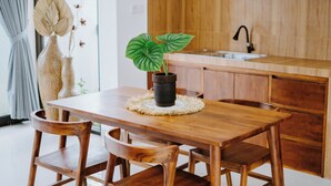 A wooden dining table with chairs, a potted plant, and a kitchen in the background. - Ramasita Villa by Bali Sukha (Ubud)