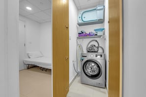 Uma lavanderia com máquina de lavar, varal e uma cama no quarto vizinho.