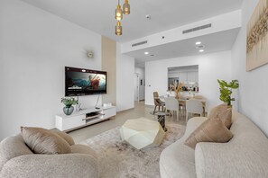 A modern living room with a flat-screen TV, a dining area, and a kitchen in the background. - Spacious 2Bedroom+ Maid room with Burj Khalifa View (دبي)