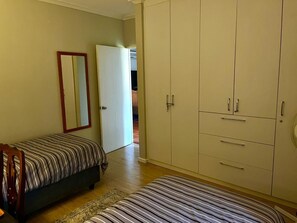 A bedroom with a bed, a wardrobe, a mirror, and a door leading to another room.