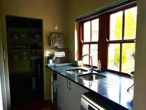 Une cuisine équipée d’un évier encastré, d’une fenêtre donnant sur un espace verdoyant et d’un meuble contenant de la vaisselle.