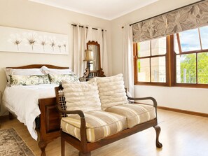Quarto com cama, cadeira de madeira, janela com vista e parede com pintura floral.