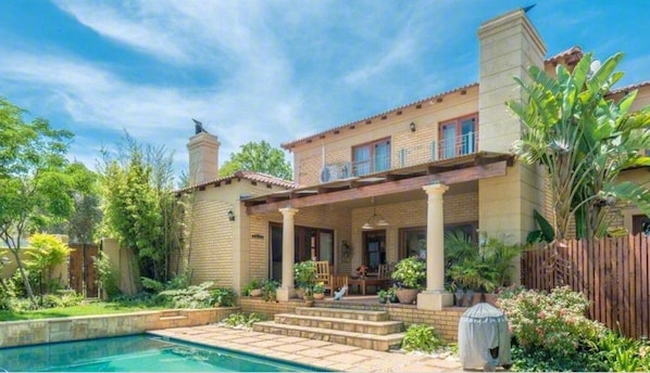 A two-story house with a pool, a covered patio, and a garden.