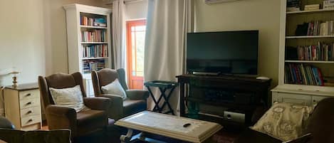 A living room with a flat-screen TV, leather armchairs, a coffee table, and bookshelves.