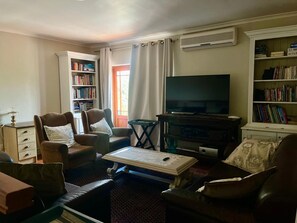 A living room with a flat-screen TV, leather armchairs, a coffee table, and bookshelves.