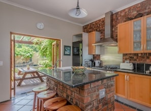 A kitchen with a brick island, wooden stools, and a view of the outdoors.