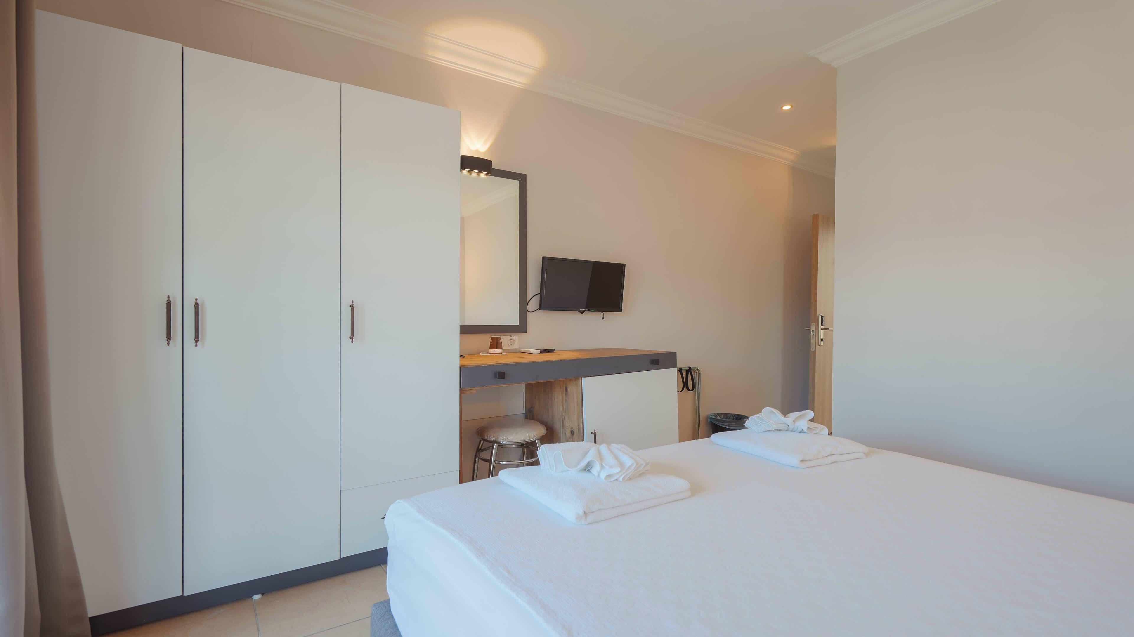 Habitación de hotel con cama, escritorio, televisor de pantalla plana, armario y espejo.