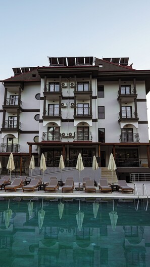 A multi-story hotel with balconies, air conditioning units, and a pool area with sun loungers and umbrellas.