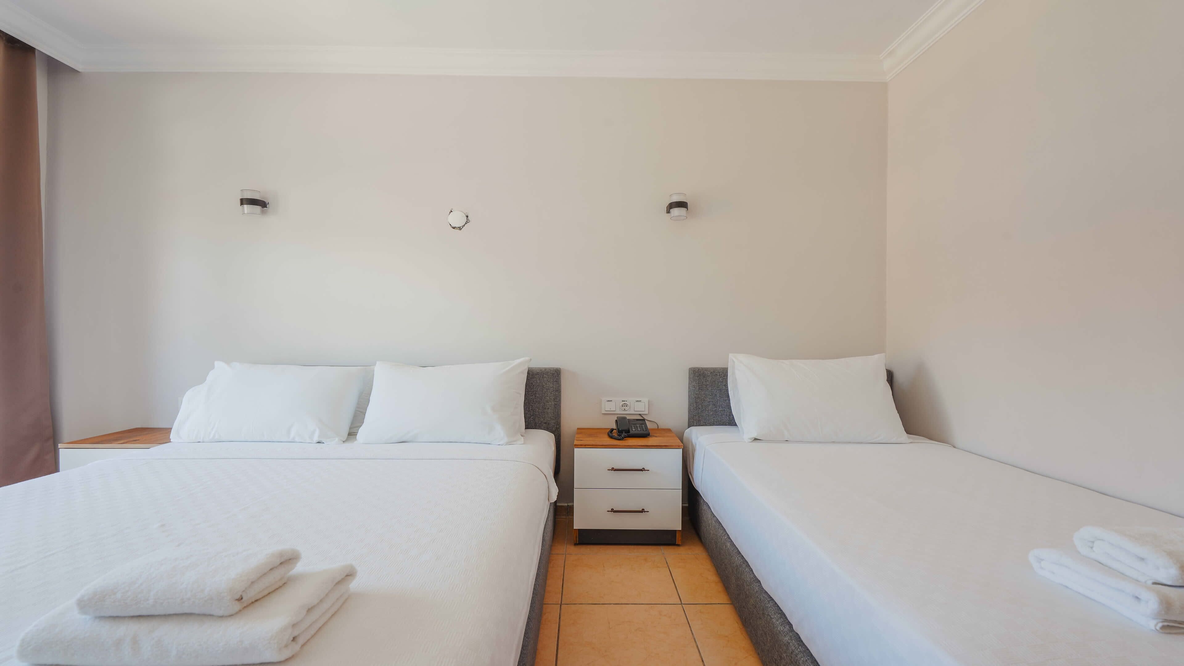 Una habitación de hotel con dos camas, una mesita de noche con un teléfono y un aplique de pared.