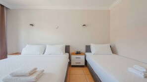 A hotel room with two beds, a bedside table with a phone, and a wall-mounted light fixture.