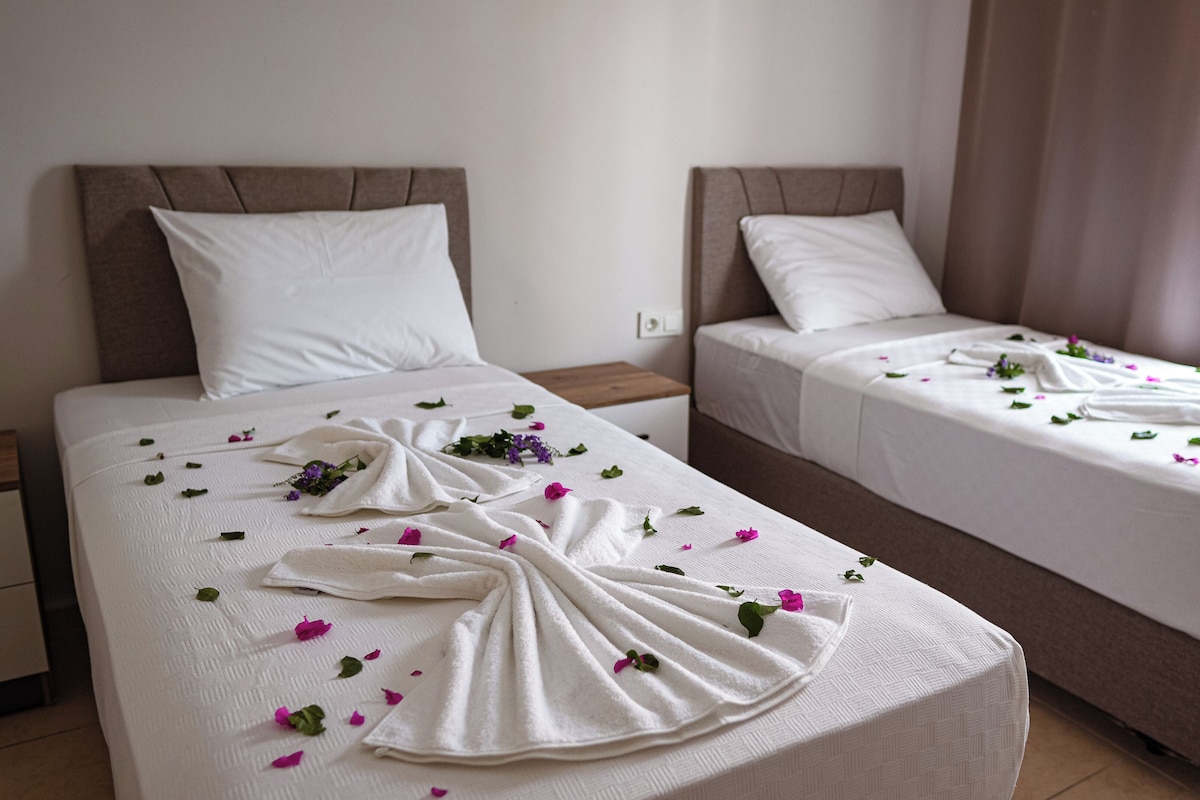 Two single beds with white linens, pillows, and a towel draped over the bed.