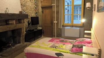 Ein Schlafzimmer mit Steinwand, Holztür, Fenster mit Aussicht, Kamin und Bett mit floralem Überwurf.