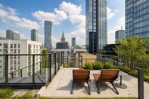 A rooftop terrace with two wooden benches, a glass balustrade, and a view of modern buildings. - Chmielna Duo Elegant | Warsaw Center & Parking (Warszawa)