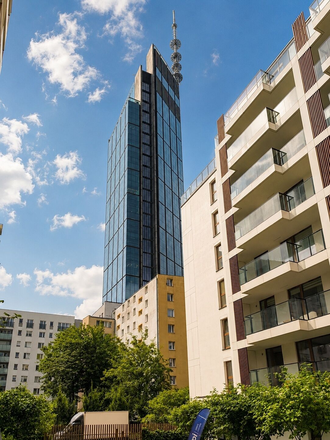 A modern high-rise building with a glass facade, surrounded by other residential buildings.