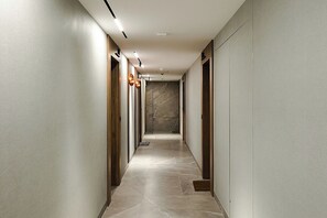 Un corridoio con pavimento piastrellato, porte in legno e illuminazione a incasso.