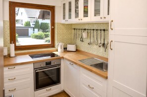 Cocina con armarios blancos, encimera de madera, horno empotrado, fregadero y ventana con vistas al exterior.