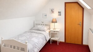 Un dormitorio con techo inclinado, una cama individual con colcha estampada, una mesita de noche con lámpara y una puerta.