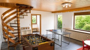 Una habitación con mesa de futbolín, mesa de ping pong y una escalera en espiral.