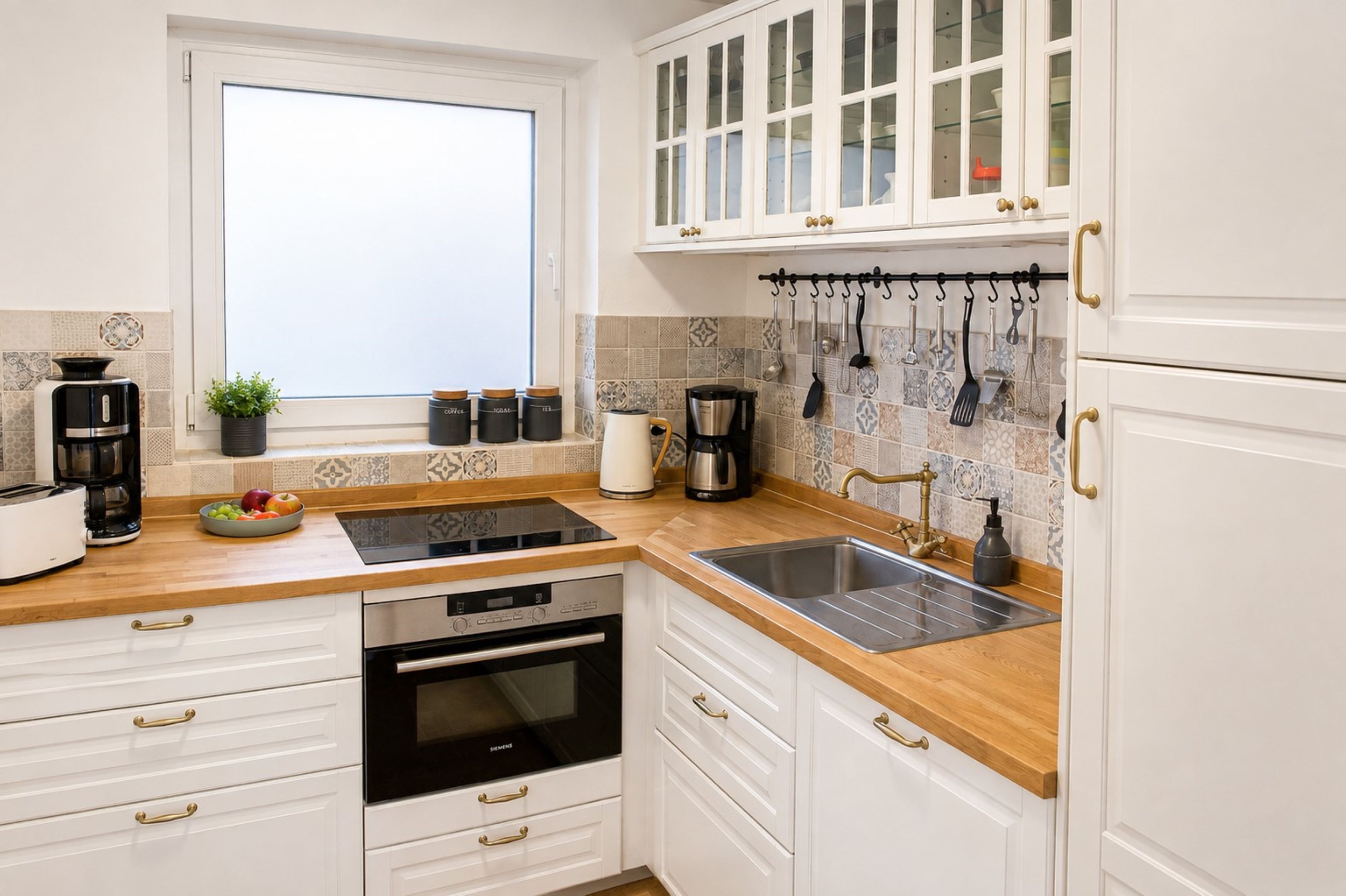 A modern kitchen with white cabinetry, a built-in oven, a dishwasher, a sink, and a window.
