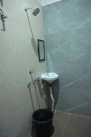 Ein Badezimmer mit Dusche, Waschbecken und einem schwarzen Eimer.