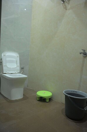 A bathroom with a toilet, a small green stool, and a bucket. - Preksha Palace (Ayodhya)