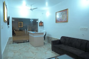 A living room with a sofa, a small table, a reception desk, and a ceiling fan. - Preksha Palace (Ayodhya)