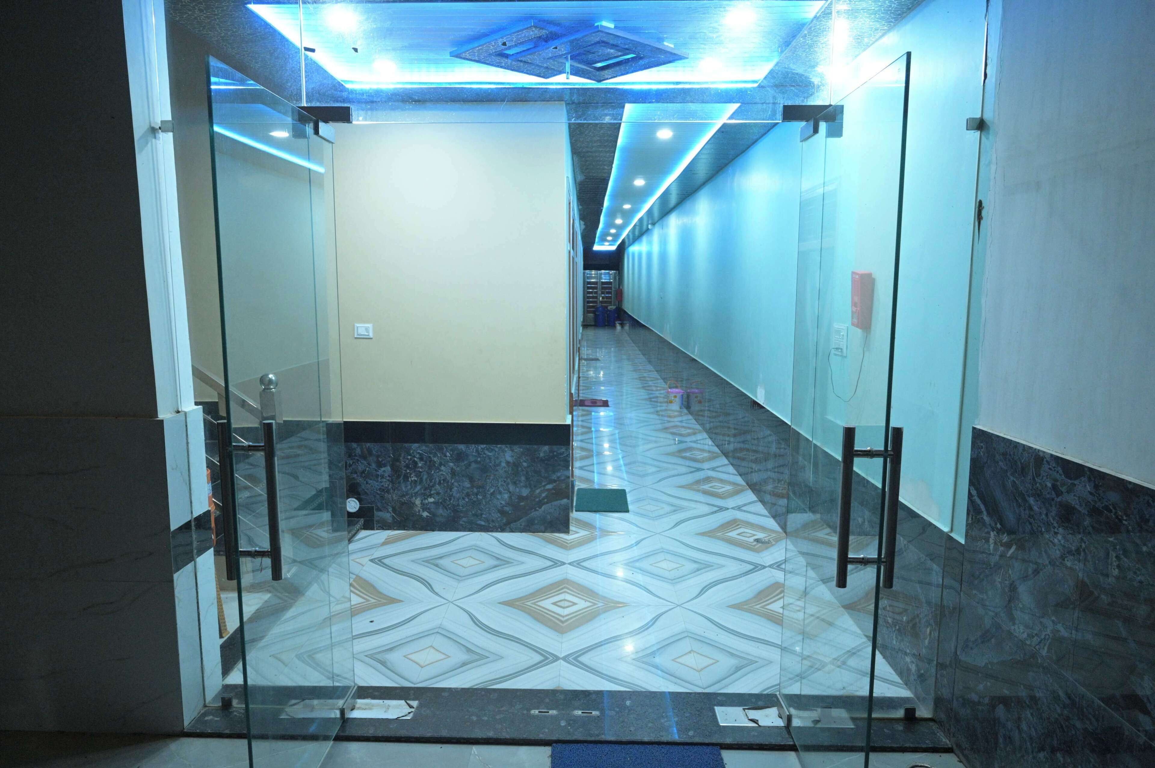 Un pasillo con puertas de vidrio, baldosas de suelo estampadas e iluminación empotrada en el techo.