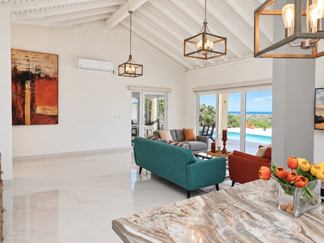 A spacious living area with a teal sofa, a red armchair, and a marble coffee table. There is a large window offering a view of the outdoors.