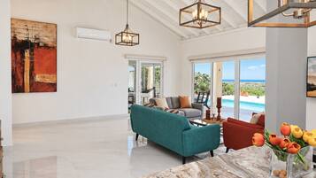 A spacious living area with a teal sofa, a red armchair, and a marble coffee table. There is a large window offering a view of the outdoors.