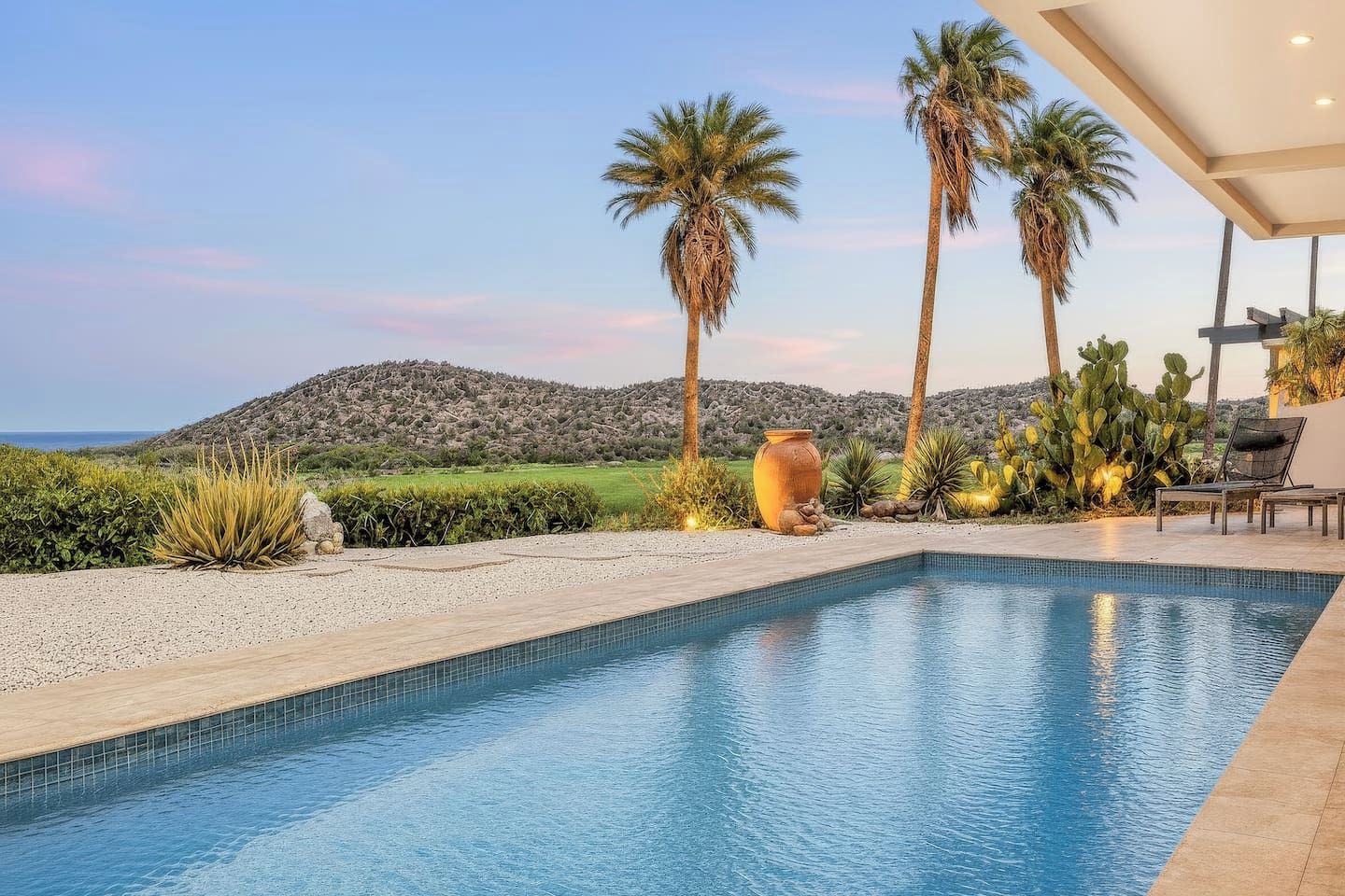 Una piscina con vistas a un paisaje montañoso, rodeada de palmeras y plantas del desierto.