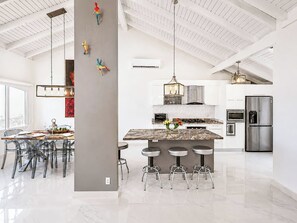 Cozinha moderna com ilha central, banquetas e área de jantar com cadeiras.