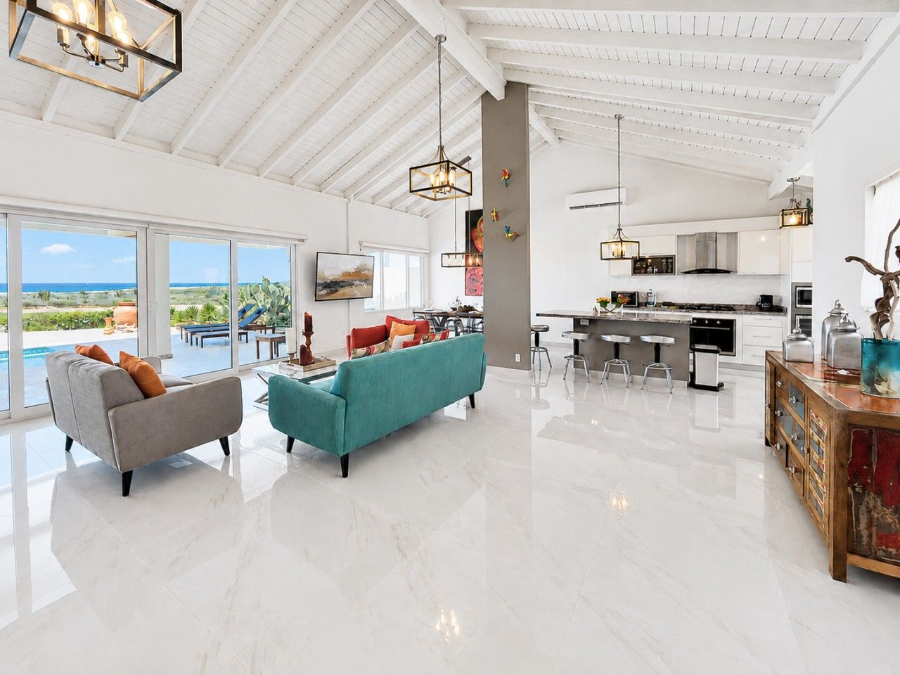 A spacious living area with a large window, a sofa, a coffee table, and a kitchen in the background.