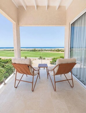 Un balcón con dos sillas y una pequeña mesa, con vista a un campo de golf y al océano.
