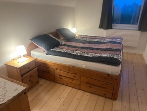 A bedroom with a wooden bed, bedside tables, a nightstand, and a window with curtains.