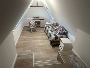 Une pièce aux dimensions réduites, avec un plafond en pente, comprenant un lit, une chaise, un bureau et une petite table.