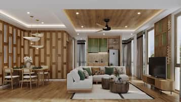 A modern living room with a sofa, coffee table, and TV. There is a dining area with chairs and a table. The room has wooden paneling on the walls and a ceiling fan.