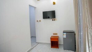 A room with a television mounted on the wall, a small wooden cabinet, and a refrigerator.