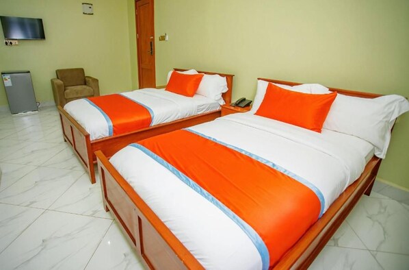 A hotel room with two wooden beds, each with white and orange bedding, a television on the wall, and a small desk with a chair.