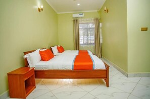 A room with a bed, a nightstand, a window with curtains, and an air conditioning unit. - Salpat Camp Lodge (Moshi)