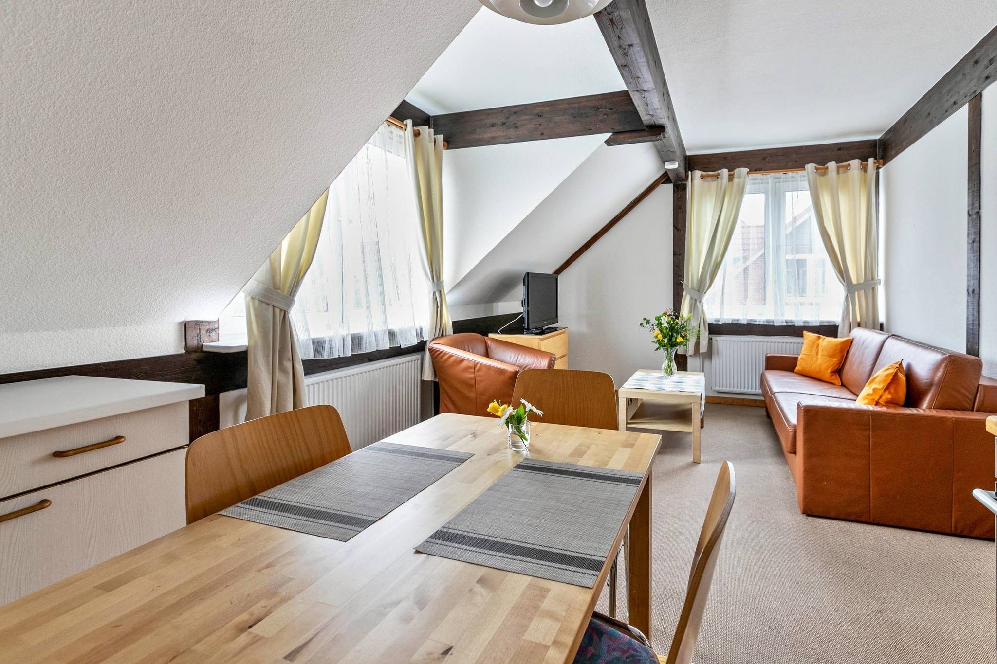 Ein gemütliches Zimmer mit einem Holzespeisetisch, einer Couch und einem Fernseher auf einem Holzgestell.