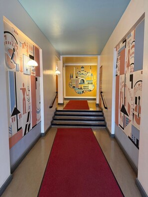 A hallway with a red carpet leading to a staircase, walls adorned with abstract art, and a light fixture on the ceiling. - Bright Design District Studio in Helsinki (Helsinki)