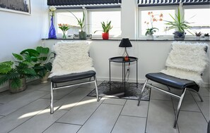 Una habitación moderna con dos sillones blancos y mullidos, una mesita con lámpara y varias plantas en macetas.