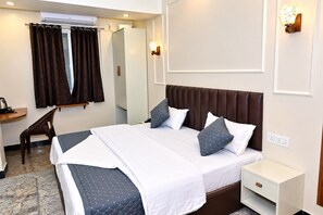 A hotel room with a bed, bedside table, and a desk with a chair. - Surya Stays (Prayagraj)