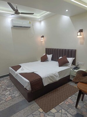 Una habitación de hotel con cama, mesita de noche, teléfono, ventilador de techo y aire acondicionado.