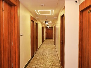 A hotel hallway with wooden doors, a tiled floor, and modern lighting fixtures. - Surya Stays (Prayagraj)