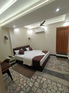 Una habitación de hotel con cama, mesita de noche y ventilador de techo.