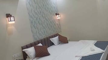 A hotel room with a bed, bedside table, lamp, and an air conditioning unit.